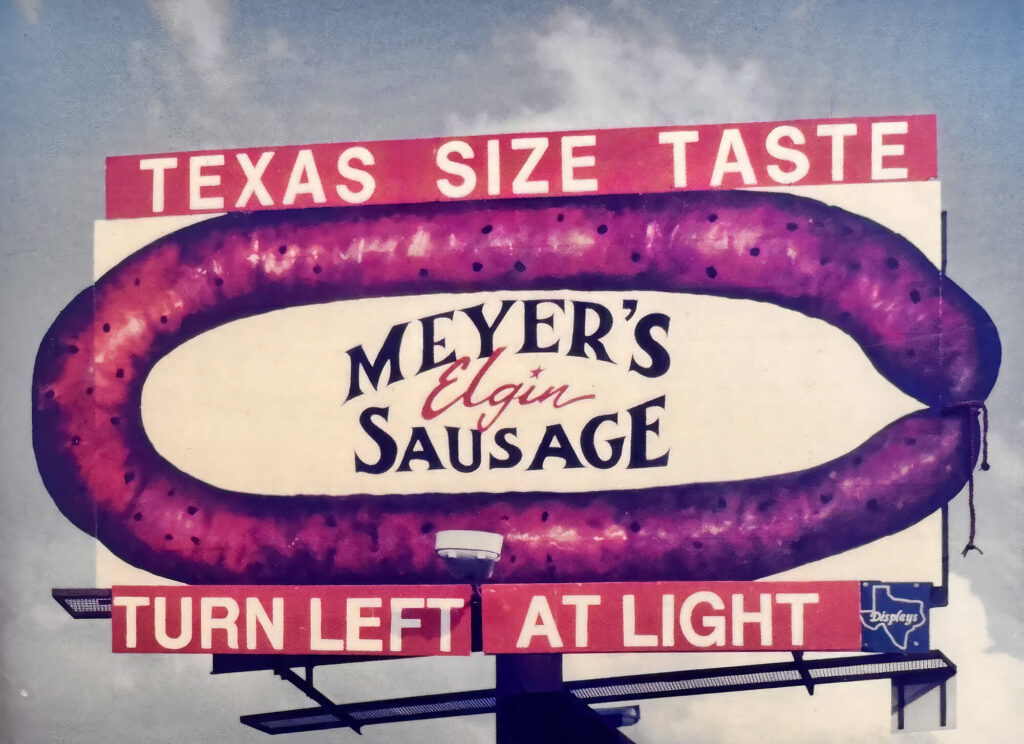 Vintage Meyer’s Elgin Sausage billboard shaped like a sausage with “Texas Size Taste” and “Turn Left at Light” signage